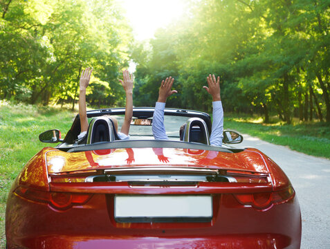 Happy free couple driving in red retro car cheering joyful with arms raised