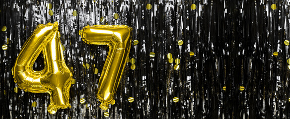 Gold foil balloon number number 47 on a background of black tinsel decoration. Birthday card,...