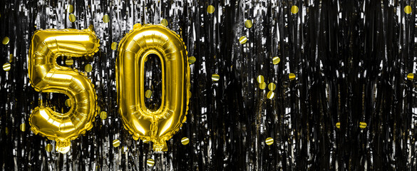 Gold foil balloon number number 50 on a background of black tinsel decoration. Birthday greeting...