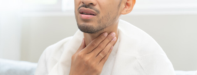 Sore throat in flu season. Young asian man touching her neck and feeling pain in throat in the...