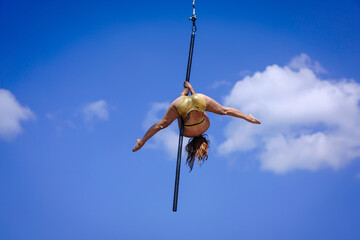 Beautiful Asian girl shows extreme advances by performing pole dance aerial in various positions and spinning stunts on the blue sky around the natural fresh and the waterfall, outdoors.
