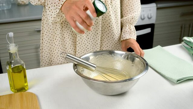 Woman cooking homemade mayonnaise sause adding salt to metal bowl on kitchen, hands close-up. Cooking sauce for salad, meat dishes. Dressing for different dishes. Culinary, cuisine concept.