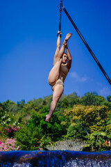 Beautiful Asian girl shows extreme advances by performing pole dance aerial in various positions and spinning stunts on the blue sky around the natural fresh and the waterfall, outdoors.