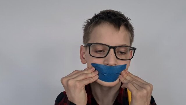 Portrait of a sad teenage boy with sticky tape on his mouth. Child rights concept and school bullying