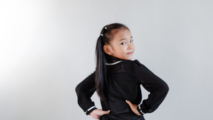 Side view of positive young Asian girl in black outfit smiling and looking at camera while standing...