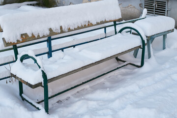 wooden bench snow next to an apartment building.