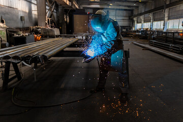 The welder works in the workshop. The moment of welding of metal structures. Beautiful sparks during welding of various metal elements in the workshop. The welder is working hard. - 702244219