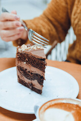 vertical image of hand of unrecognizable woman cutting slice of chocolate cake with fork