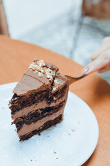 vertical image of hand of unrecognizable woman cutting slice of chocolate cake with fork