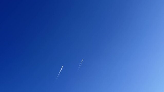 Two airplanes with jet contrails crossing the clear and blue sky. Cloudscape.