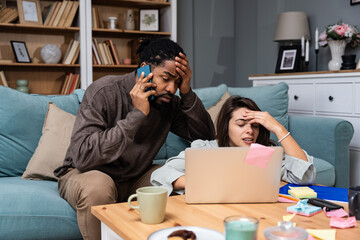 Young freelance mixed-race couple small business owners working in home office on laptop computer,...