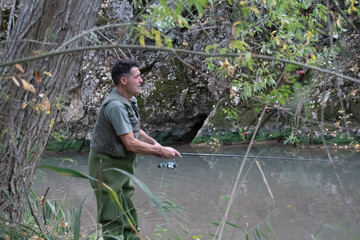 Fisherman in a vest and waders in the river casting and retrieving his fishing rod.