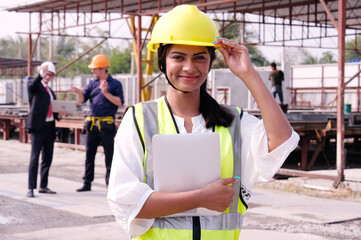 Female engineer wearing safety helmet stands smiling at construction site.