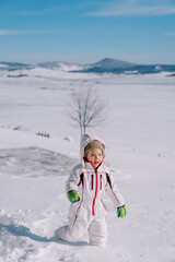 Fototapeta na wymiar Little smiling girl walks through deep snowdrifts in a mountain valley