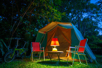 vintage cabin tent,  Antique oil lamp on a wooden table with retro chairs. at night in the  forest