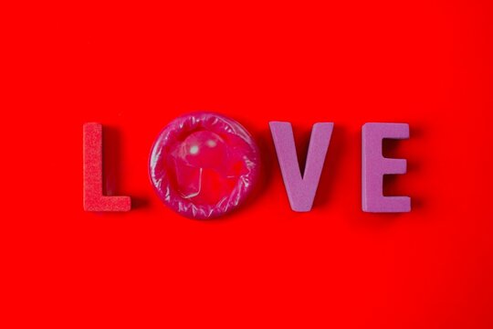Love lettering with condom on red background. Educational safe sex and STD prevention concept.	