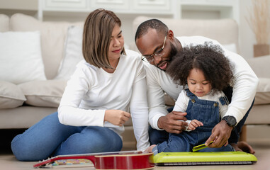 Adorable kid girl playing keyboard with multiethnic family at home. Afro curly hair multiracial...