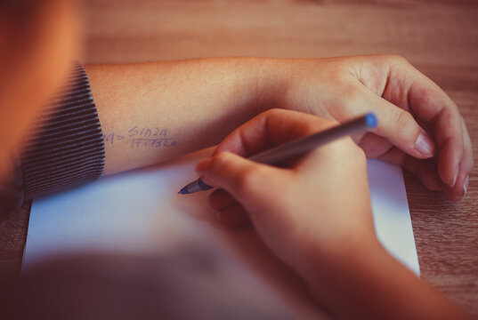 Student cheating during exam in university, reading cheat sheet with formula written on hand