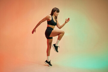 Fototapeta na wymiar Standing on the one leg, side view. Young woman in fitness clothes is in the studio
