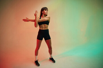 Fototapeta na wymiar Standing and doing exercises. Young woman in fitness clothes is in the studio