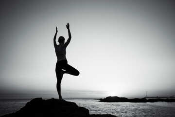 Silhouette of a yoga woman practicing on the shore. Black and white photo.