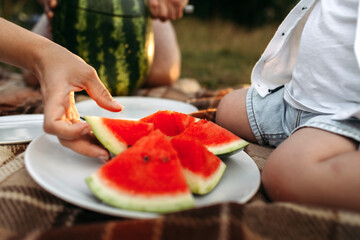 A woman takes a ripe triangular slice of watermelon from a white plate.