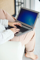 Fototapeta premium Relaxed young girl sitting in chair at home with laptop computer on her laps, close up of the female hands.