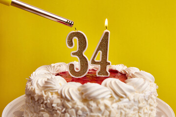 A candle in the form of the number 34, stuck in a holiday cake, is lit. Celebrating a birthday or a...