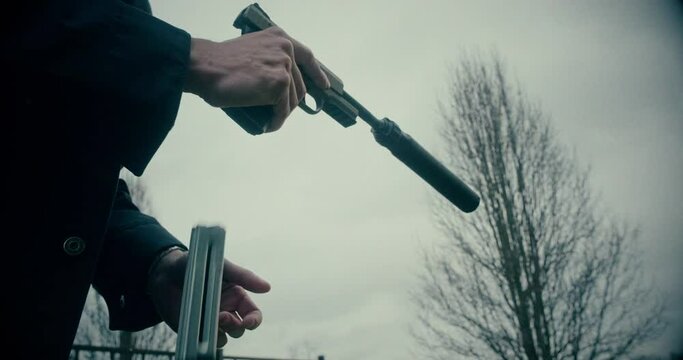 Slow Motion shot of  Man reloading suppressed 22 caliber pistol with snow falling around him
