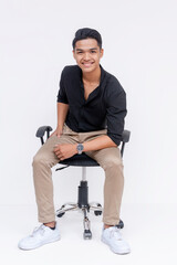 A confident and handsome Filipino man sitting relaxed on an office chair. Studio shot isolated on a...