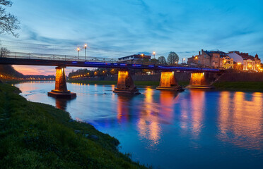Beautiful view of the night city, in the foreground there is a river and a pedestrian bridge