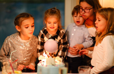Group of joyful little kids celebrating birthday party and blowing candles on cake