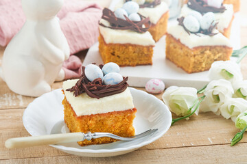Easter carrot cake bars decorated with chocolate nest and chocolate candy eggs blossoming cherry or apple flowers on rustic light wooden backgrounds. Easter holiday meal. Traditional Easter food.