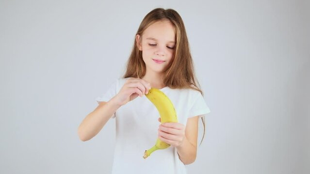 Cute child girl eating banana. Preteen girl peeling and eating banana, white background