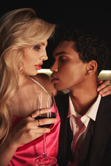 appealing blonde woman with glass of red wine looking sensually at her african american boyfriend