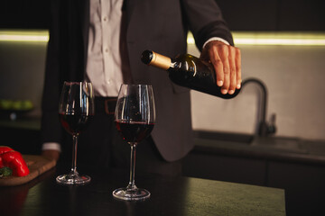 cropped view of young african american man in elegant chic suit pouring red vine into glasses