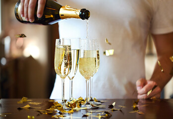 Champagne Flutes In Golden Sparkle Background with golden confetti. Man pouring sparkle wine