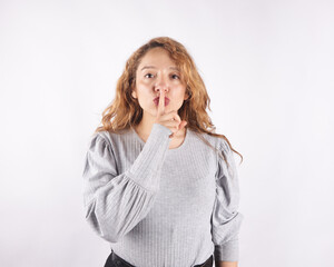 Photograph of white latin woman on light background making gestures of silence. Concept of emotions and sensations.