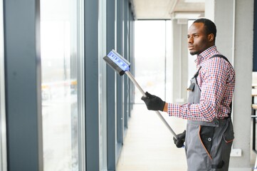 African Male professional cleaning service worker in overalls cleans the windows and shop windows...