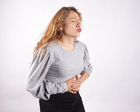 Photograph of white latina woman on light background making stomach pain gestures.