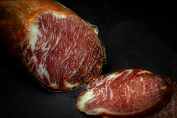 Close up view of cut of delicious Iberian lomo embuchado sausage cured in winery in Spain on black...