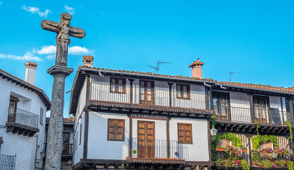 Crucero de piedra y casas tradicionales con balcón lleno de macetas y tiestos en la hermosa villa...