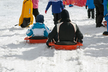 Young people sitting in sledges to run down the slope.