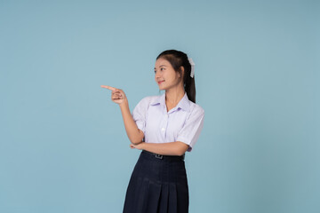 Asian female high school student pointing and looking Used for displaying websites or posters. Educational presenter of Institutes and tutoring schools Taking photos in a studio with a blue background