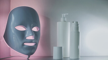Light therapy LED mask on a shelf next to facial skin care products.