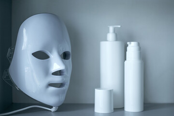 Light therapy LED mask on a shelf next to facial skin care products.