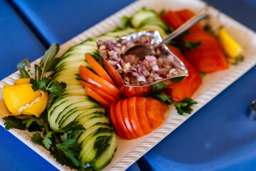 selection of garnishes, sliced cucumbers tomatoes parsley and chopped red onion on a white platter 