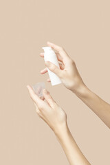 A womans hands holding a white cosmetic bottle on a beige background