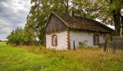 Fototapeta na wymiar Stara, opuszczona, zarujnowana chatka z bialymi scianami i dachemn z gontów