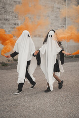 Couple wearing cute ghost robes playing with colored smoke